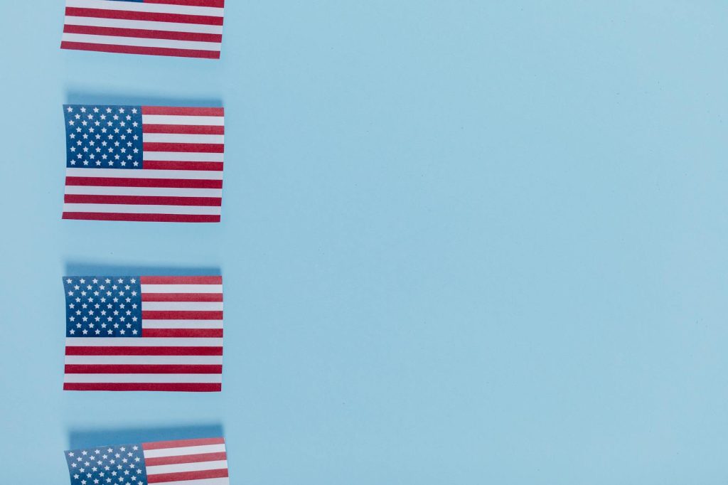 Four American flags aligned on a light blue background with copy space.