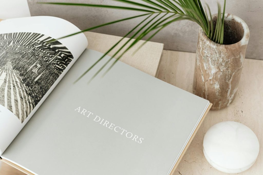 Open art book beside a decorative marble vase and palm leaf, showcasing modern aesthetics.