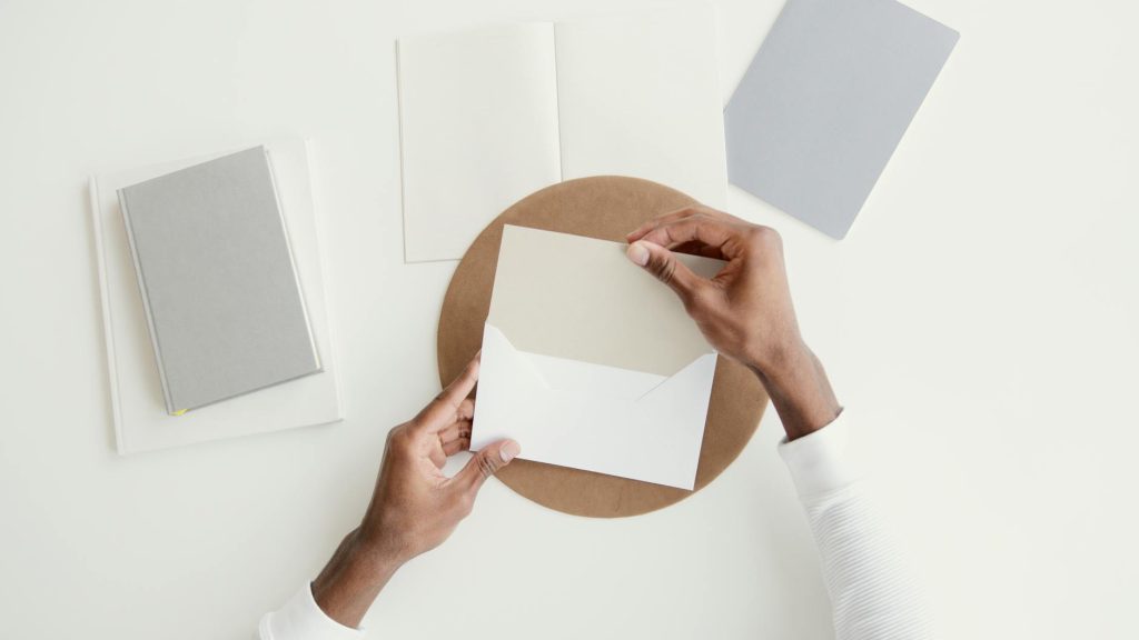 A minimalist overhead shot of hands opening an envelope on a clean desk with open notebooks.
