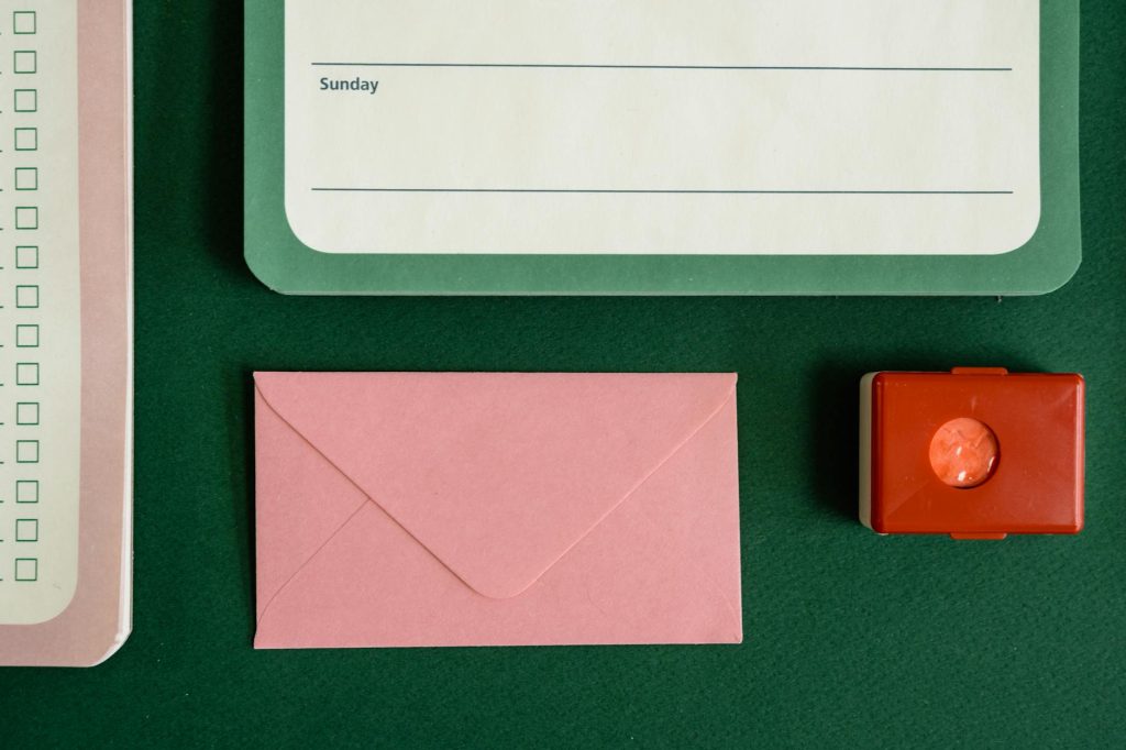 Flat lay of notepad, envelope, and stamp on a green surface.