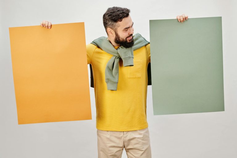 Bearded man in yellow shirt holding blank orange and green posters with copyspace.