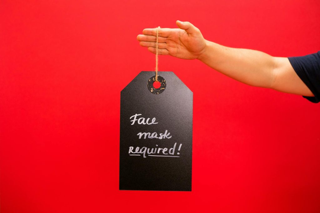 Hand holding a sign with 'Face mask required' message against a bright red background.