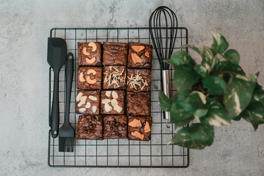 A top view of homemade brownies on a cooling rack with a plant and kitchen utensils.