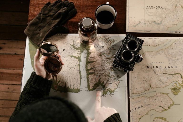 Top view of vintage exploration setup with maps, compass, gloves, and retro camera.