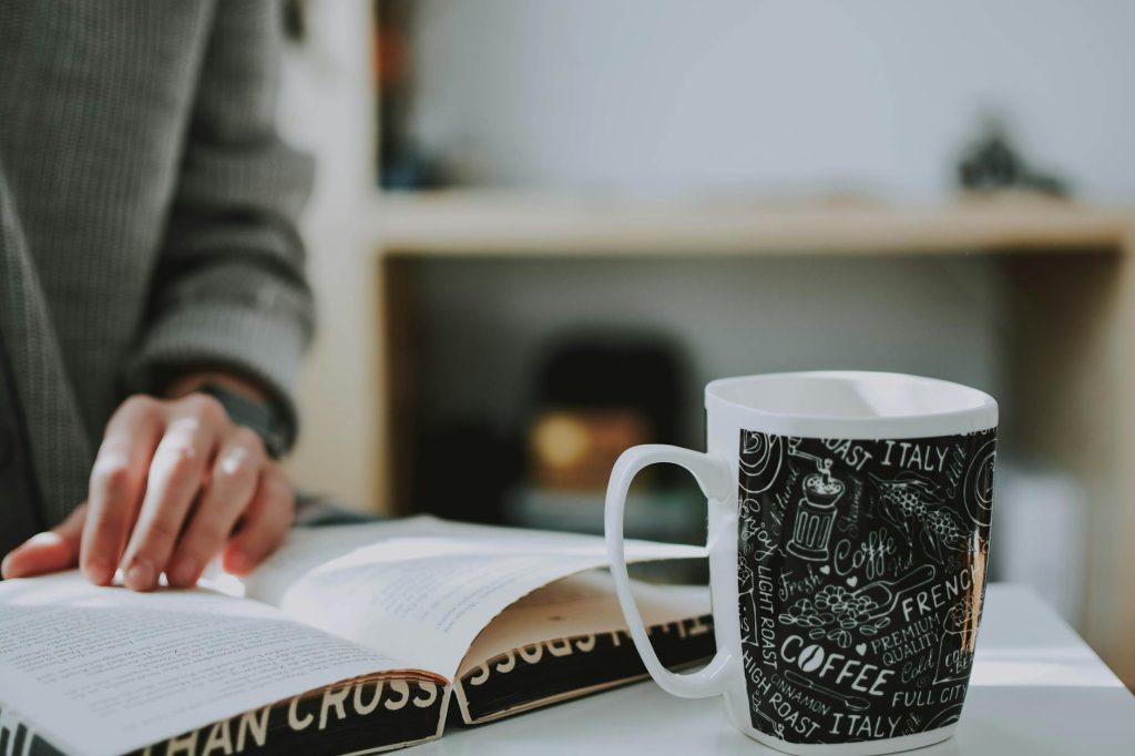 Close-up of a person reading a book with a decorative coffee mug nearby.