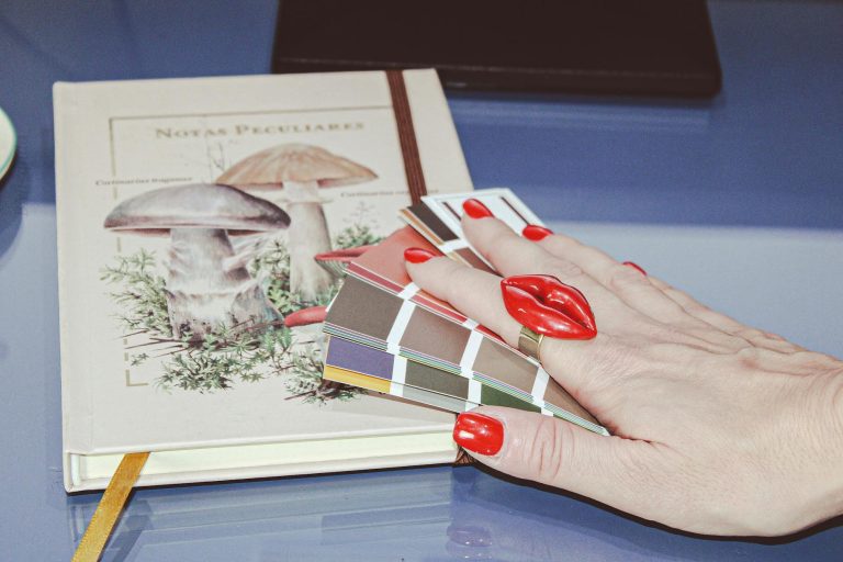 A red manicured hand displaying color swatches on a mushroom illustrated book.