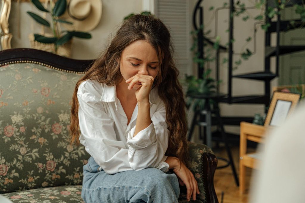 Woman in a white shirt sitting thoughtfully on a vintage sofa indoors.