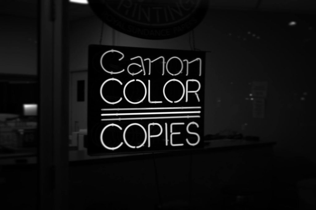 A black and white photo of a neon sign reading 'Canon Color Copies' inside a shop in Raleigh, NC.