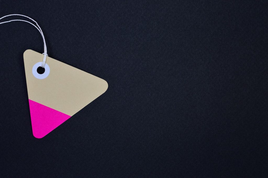 Triangular cardboard tag with vibrant pink and beige hues on a black background, perfect for design use.