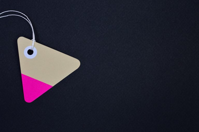 Triangular cardboard tag with vibrant pink and beige hues on a black background, perfect for design use.