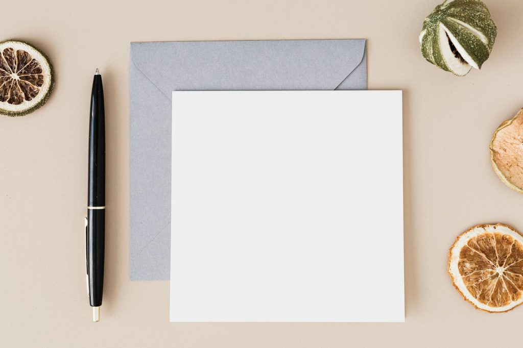 Top view of a minimalist flat lay featuring a blank paper, envelope, pen, and dried citrus slices.