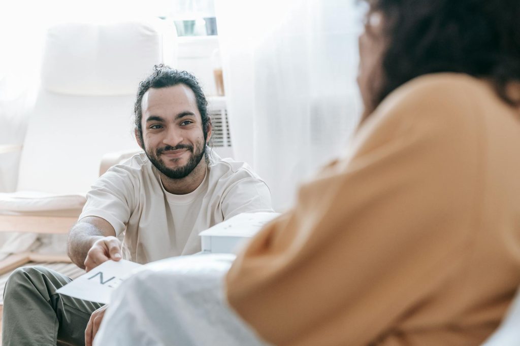 Casual indoor scene of a smiling man handing paper to a woman. Bright and relaxed ambiance.