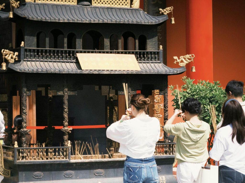 Group of people offering incense at an ornate traditional temple.