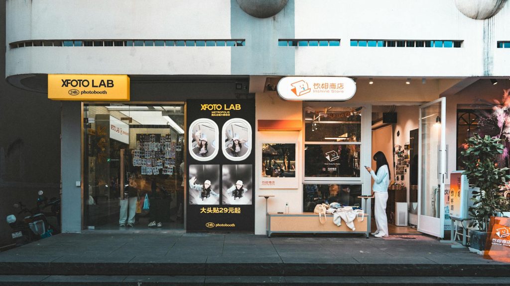 Street view of a modern photo lab storefront with a customer using a smartphone.