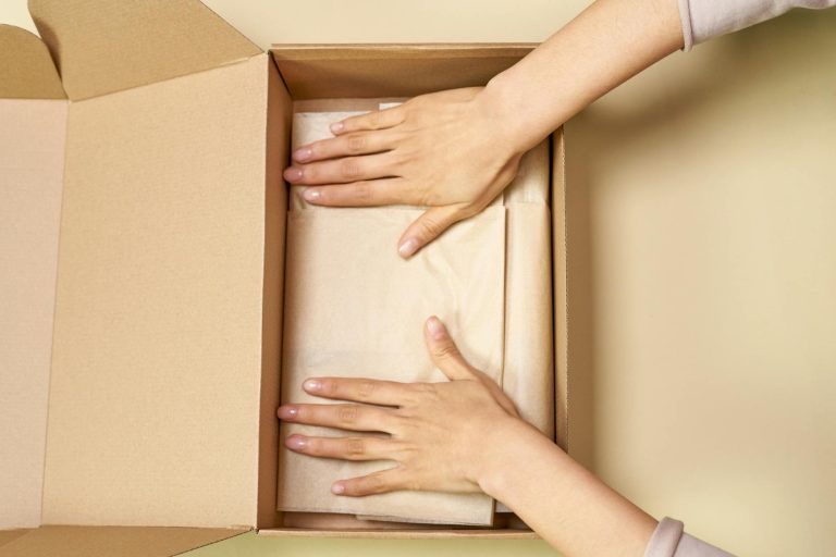 Close-up of hands packing a cardboard box with care using parchment paper.