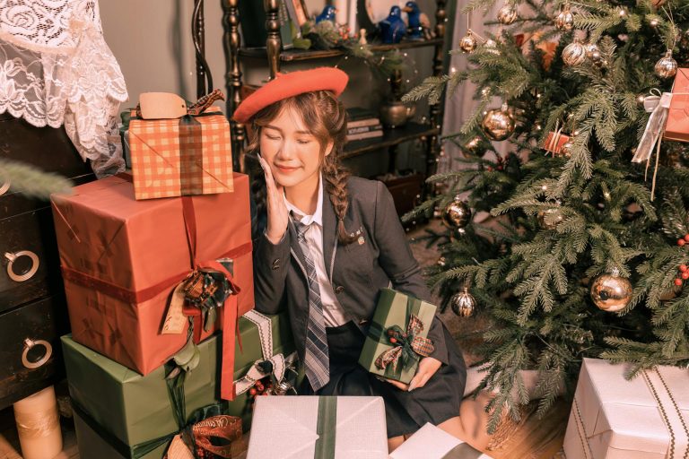 Young woman in holiday setting surrounded by Christmas gifts and tree.
