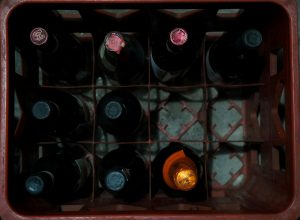 Overhead shot of assorted wine bottles in a red plastic crate showcasing storage arrangement.