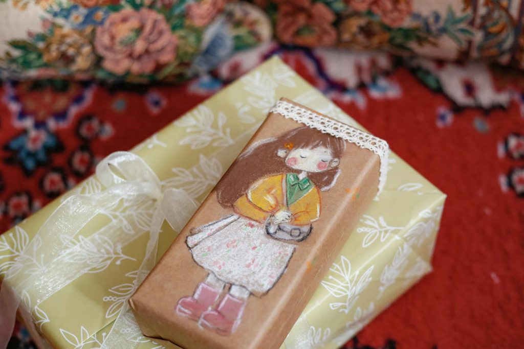 Colorful hand-painted gift box on decorative rug, featuring cute illustration.