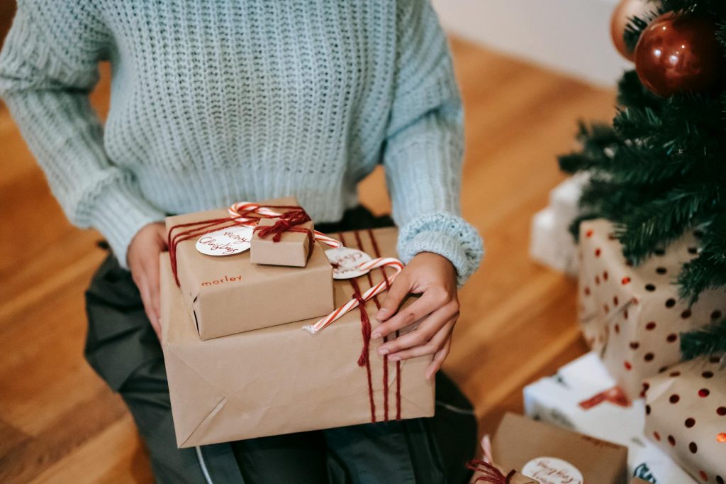 Crop unrecognizable female with heap of gift boxes sitting on floor during New Year holiday at home