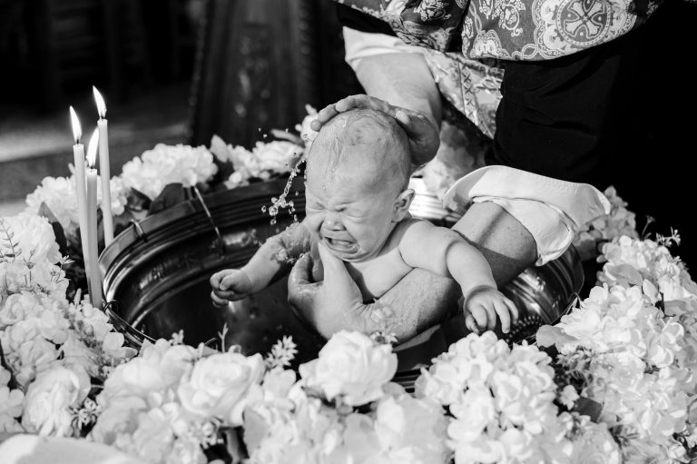 Black and white photo of a baby baptism ceremony with floral decorations.
