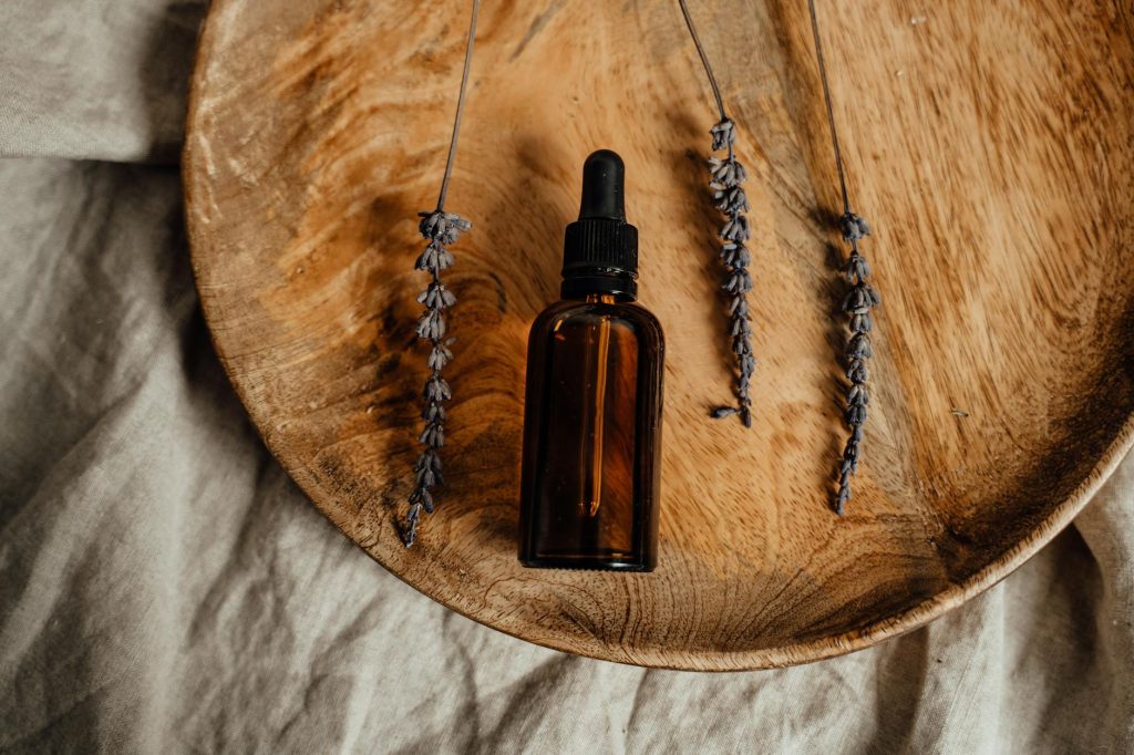 Brown glass dropper bottle with dried lavender on wooden platter, ideal for skincare promotions.