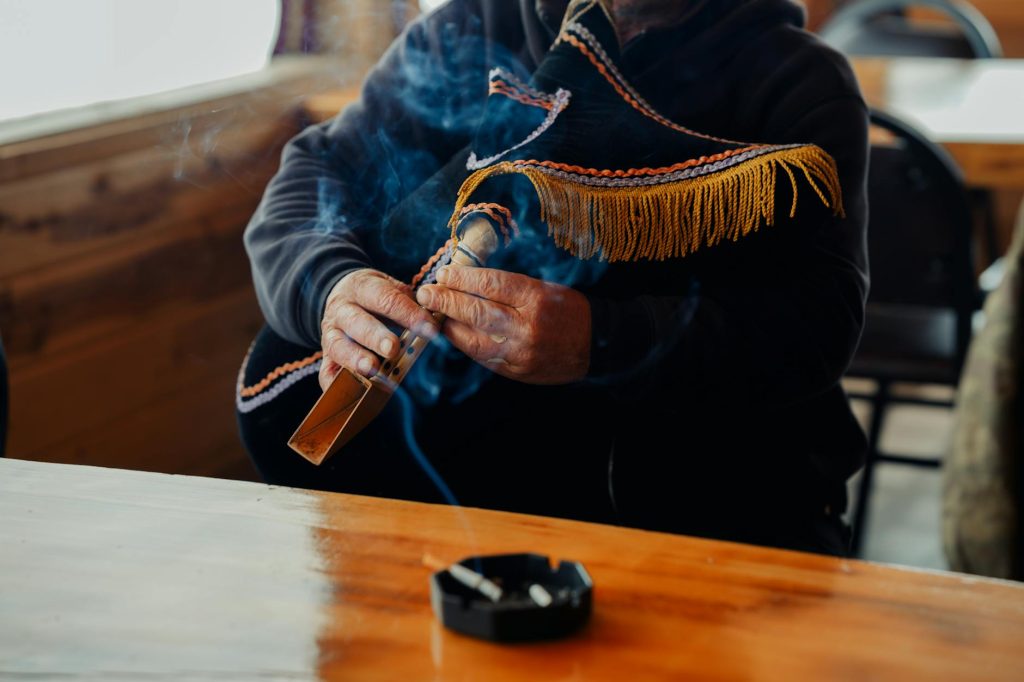 Close-up of a man smoking a pipe with fringe decoration, indoors with smoke
