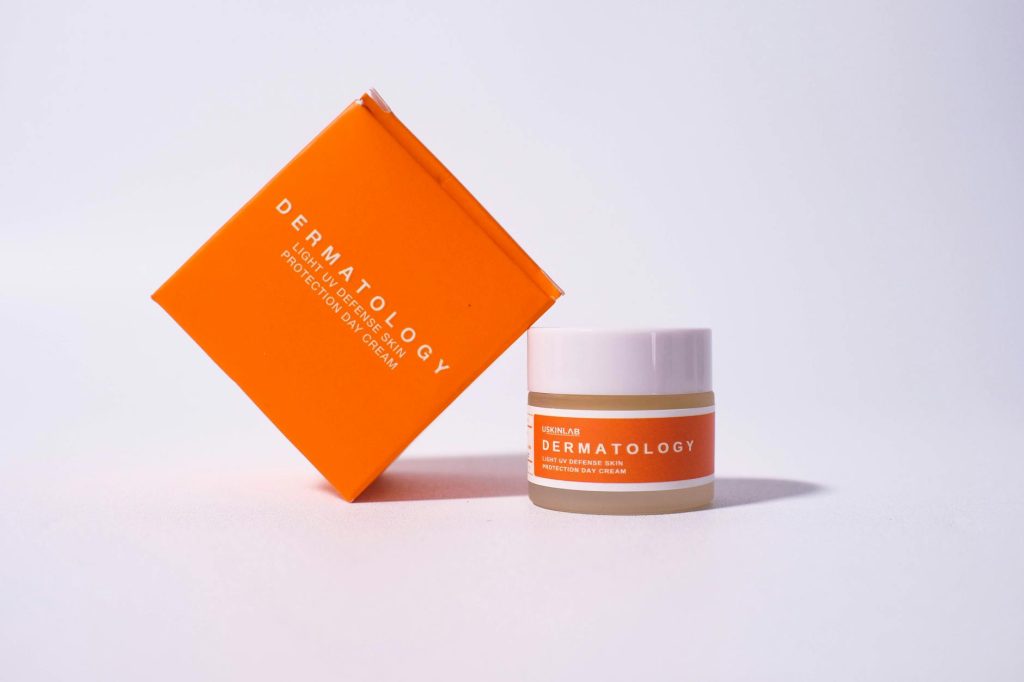 Bright orange dermatology cream packaging on white background for skincare advertisement.