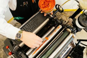 A person applying ink on a vintage Heidelberg printing press in a workshop setting.