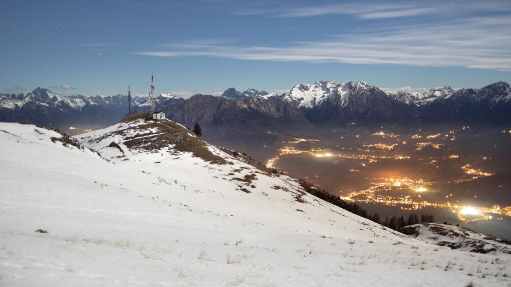 Beautiful snowy alpine mountain landscape at night with city lights in the valley.