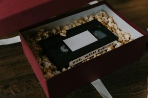 A nostalgic VHS tape resting in a popcorn-filled gift box on a wooden surface, perfect for a cozy movie night.