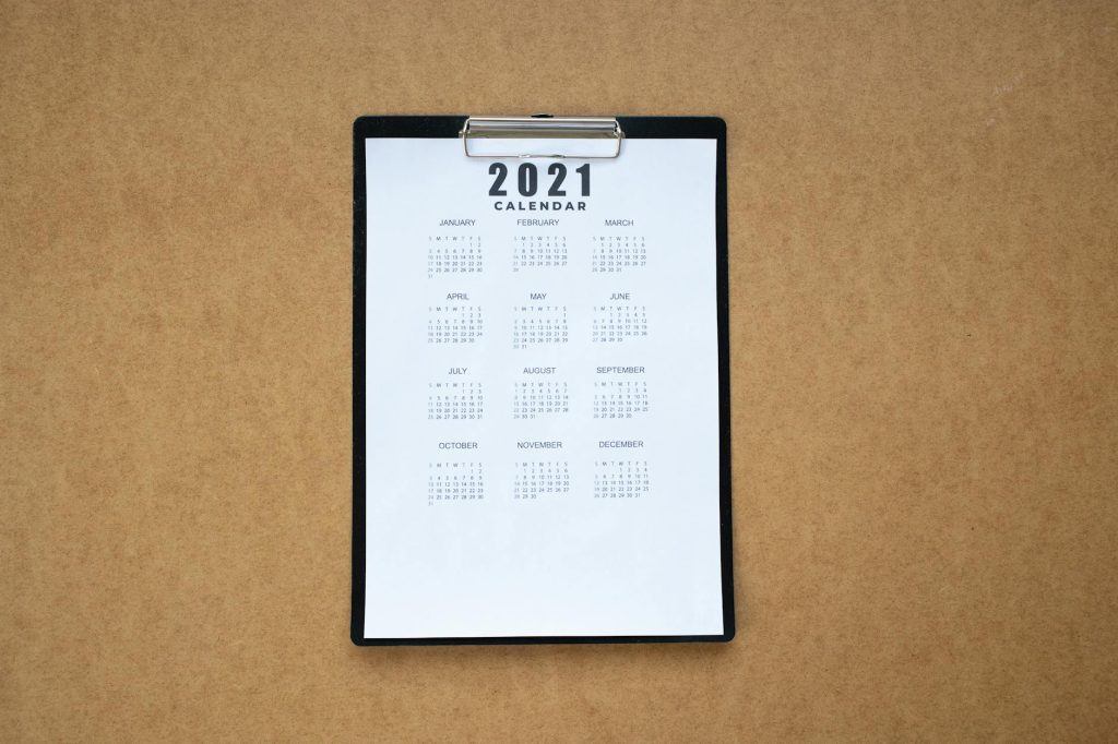 Top-down view of a minimalist 2021 calendar on a clipboard with brown background.