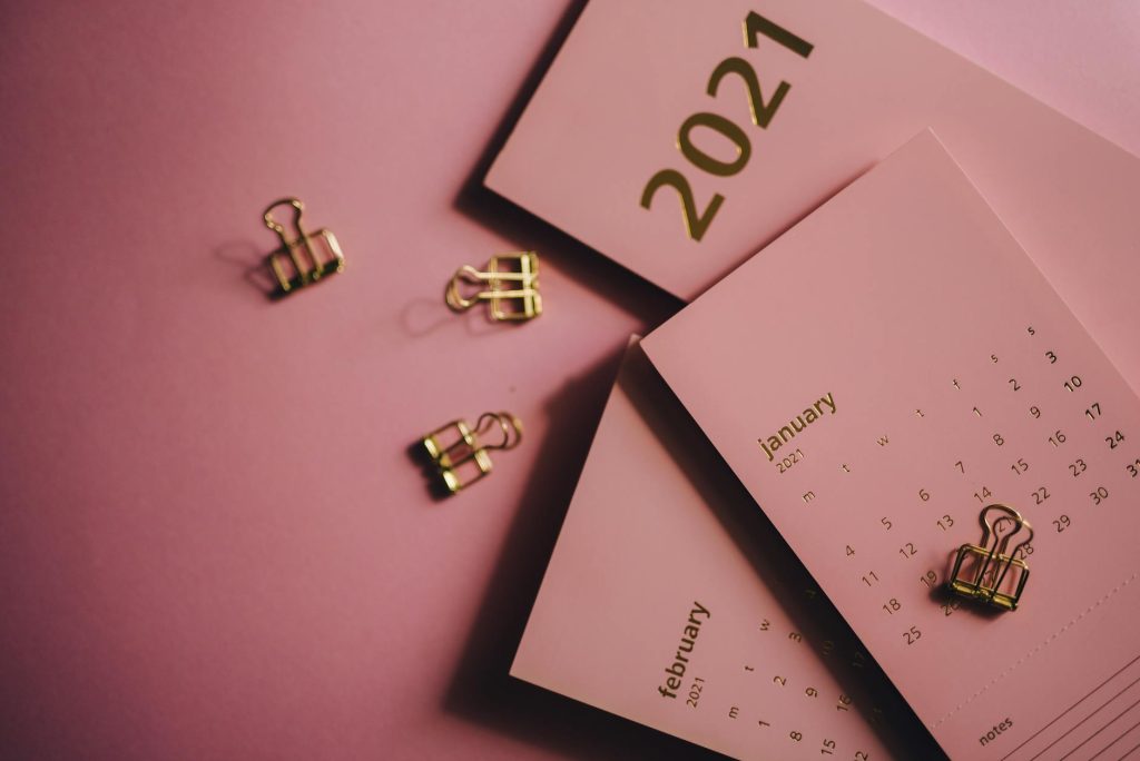 Overhead view of collection of modern monthly calendars near metal clips on pink table