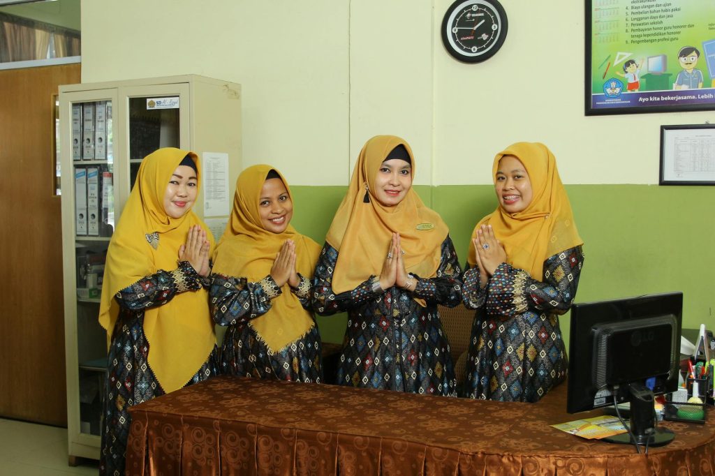 Indonesian female teachers in traditional dress standing indoors, showcasing cultural clothing.