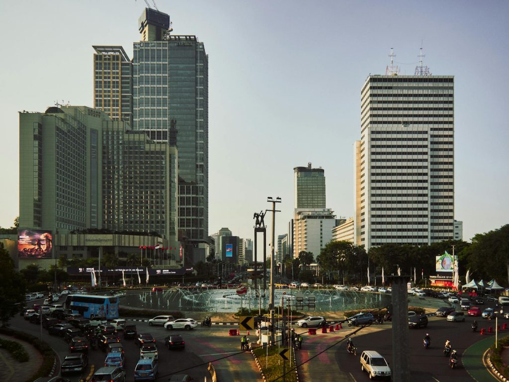 A bustling Jakarta cityscape featuring iconic skyscrapers and a central fountain during the day.
