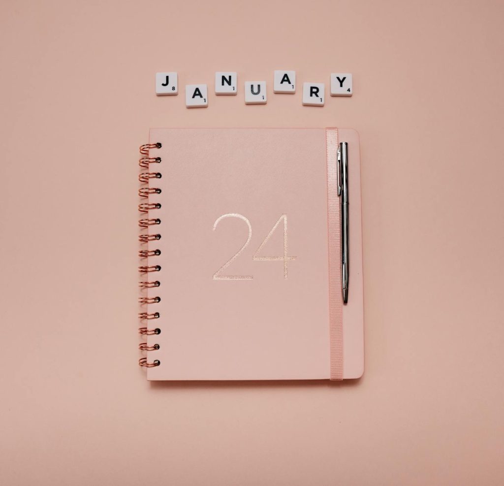 Elegant light pink planner and pen on a peach background, perfect for organizing January goals.
