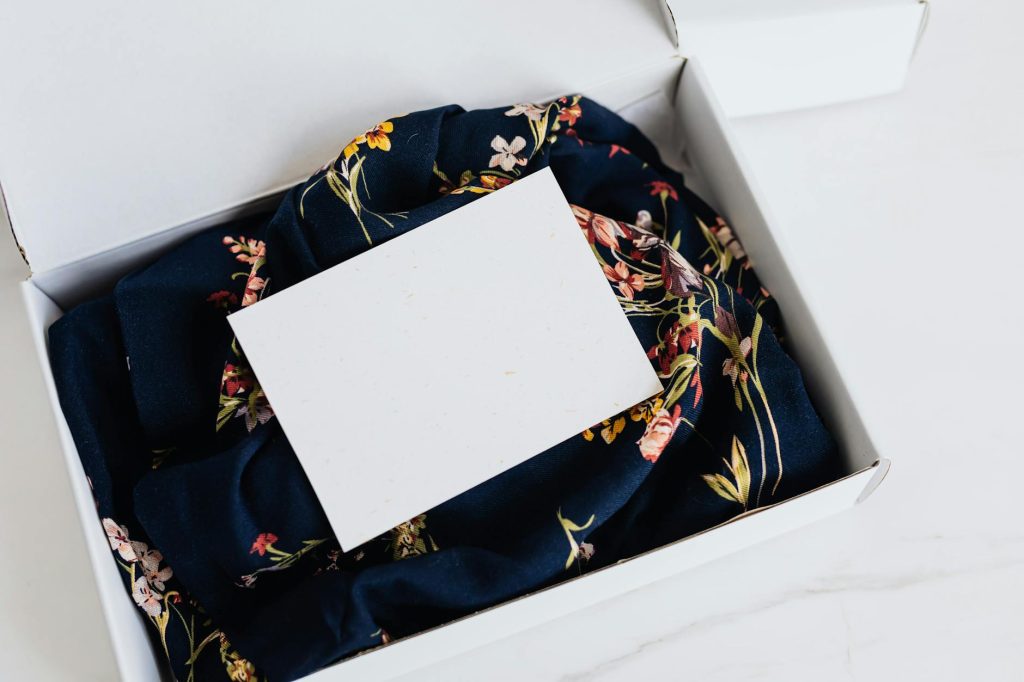 Empty business card on floral fabric inside a white gift box.