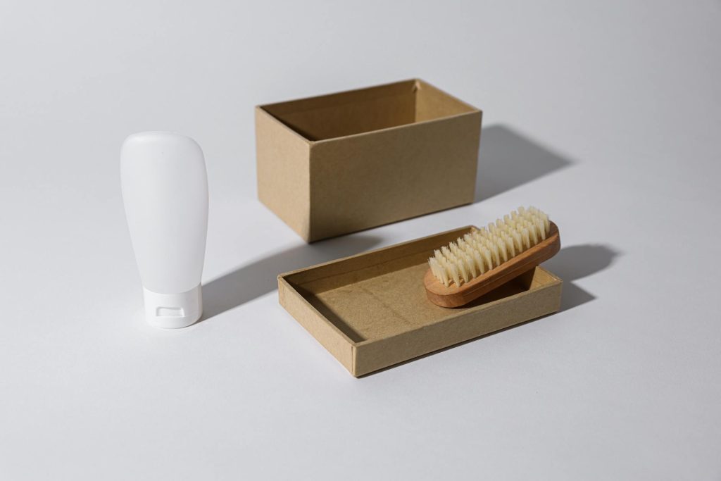 A clean, minimalist mockup featuring a cardboard box, a brush, and a white bottle, ideal for product packaging concepts.