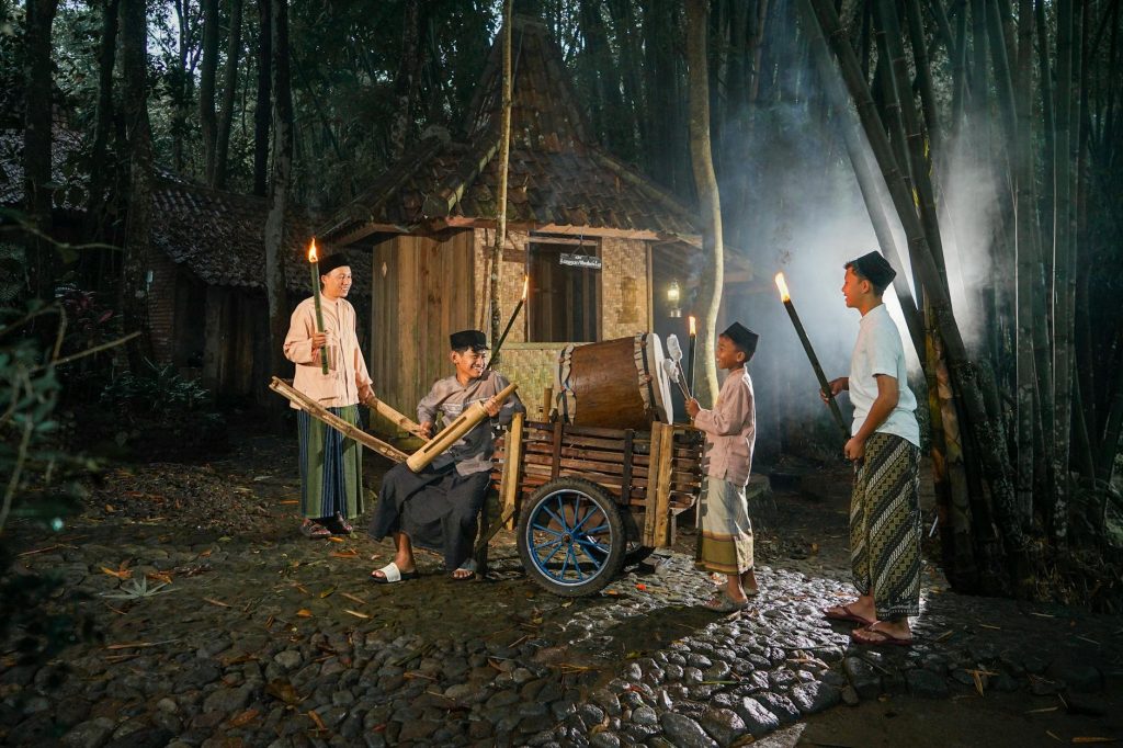 A group of adults and children perform a traditional night ceremony outdoors with drums and torches.