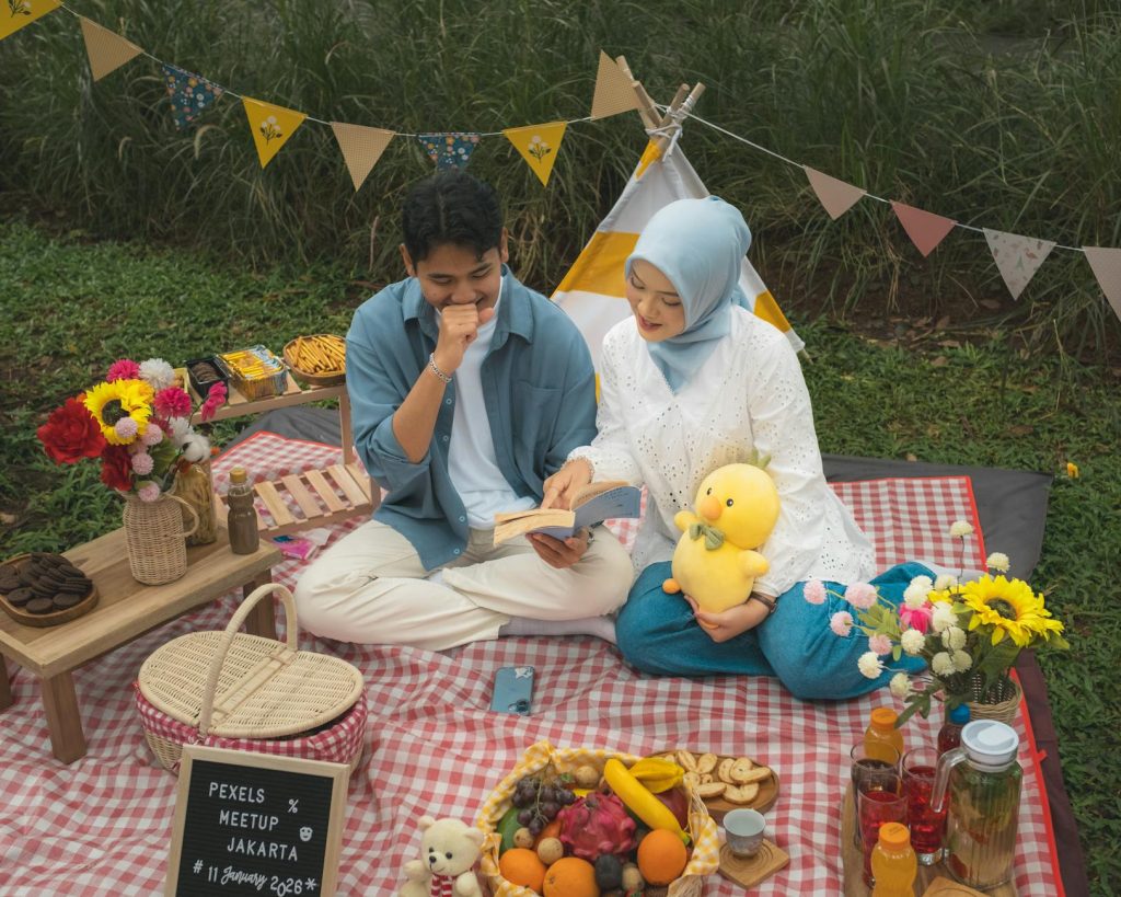 A young couple enjoys a picnic in Jakarta, reading and relaxing outdoors beside fruit and flowers.