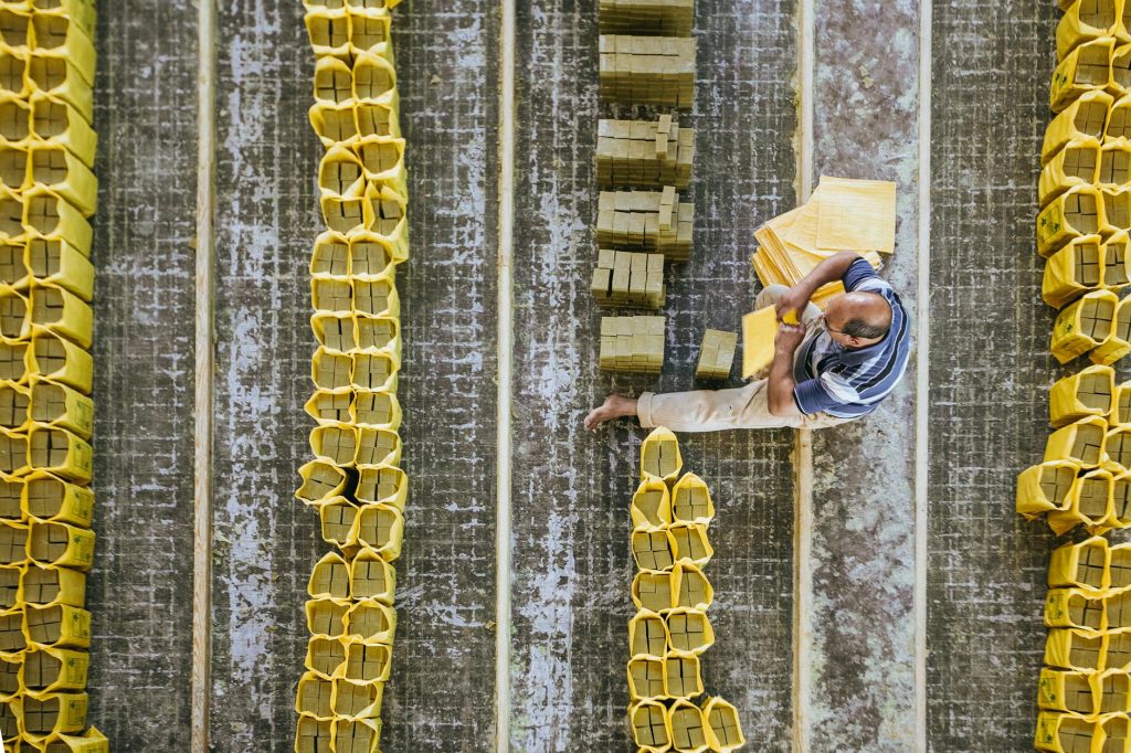 Top view of anonymous barefoot male worker sitting on floor while putting hard soap into plastic packages in production room