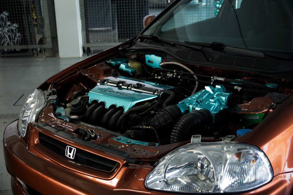 Close-up of a customized Honda engine with teal accents in an indoor workshop.