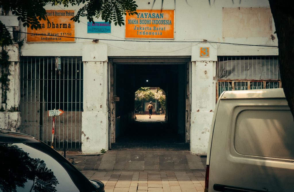 A person walks through a shaded alleyway in bustling Jakarta Barat, Indonesia.