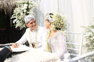 A couple dressed in traditional attire, smiling during their wedding ceremony outdoors.