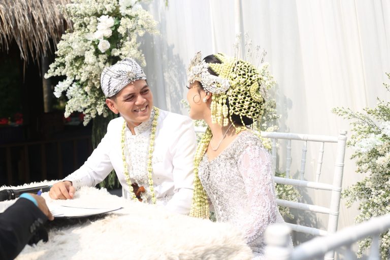 A couple dressed in traditional attire, smiling during their wedding ceremony outdoors.